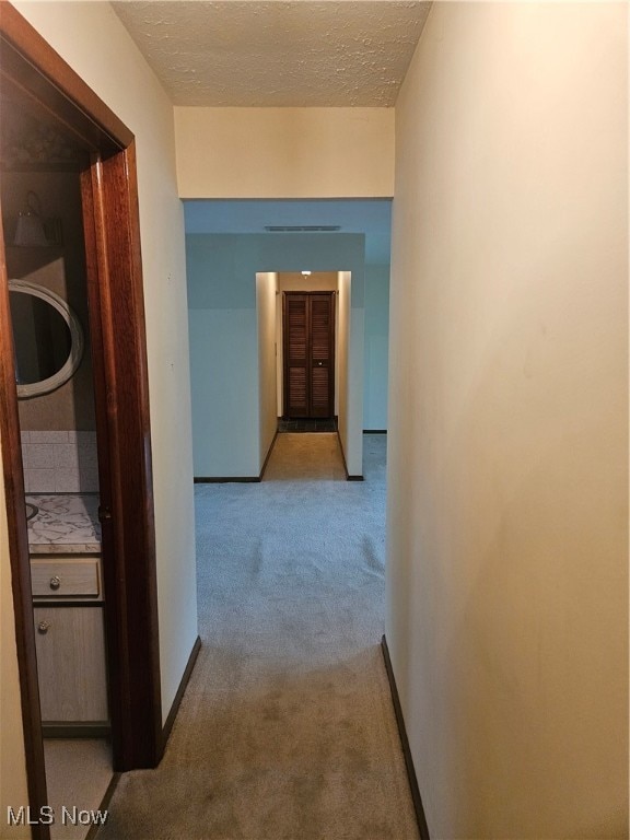 hall with a textured ceiling and light colored carpet