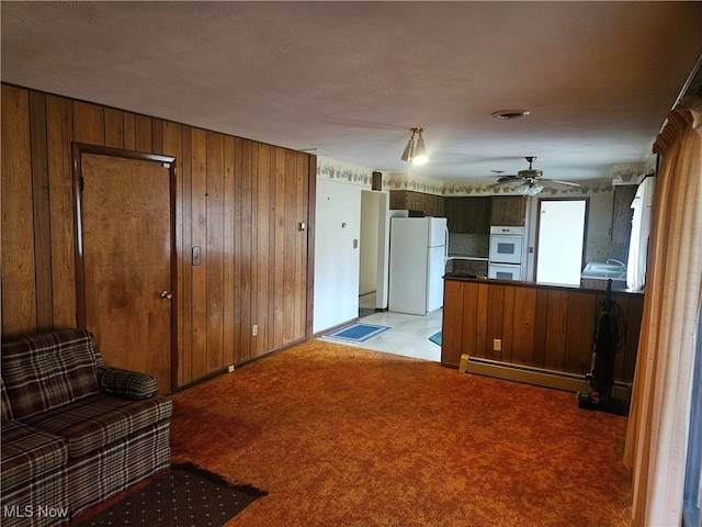 kitchen featuring wooden walls, a baseboard radiator, light carpet, and white appliances