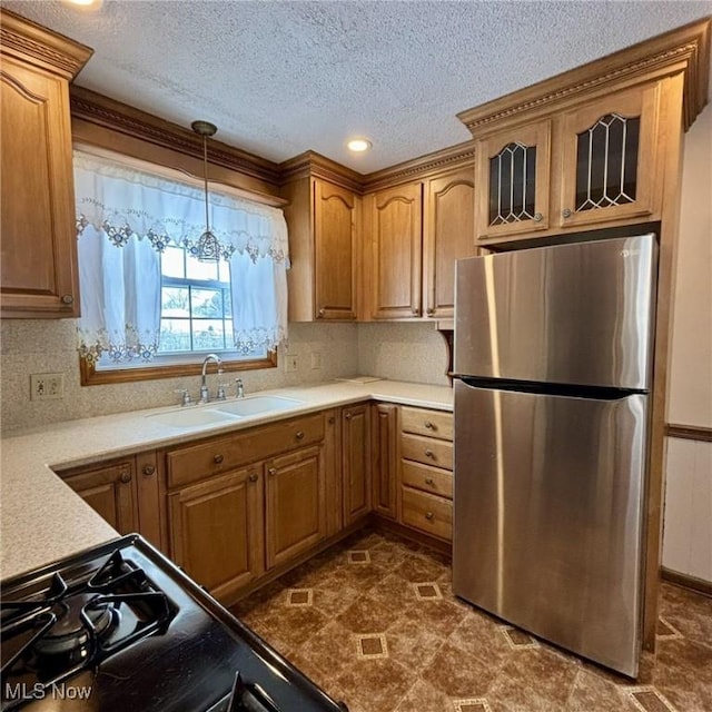 kitchen featuring pendant lighting, stove, sink, stainless steel fridge, and a textured ceiling