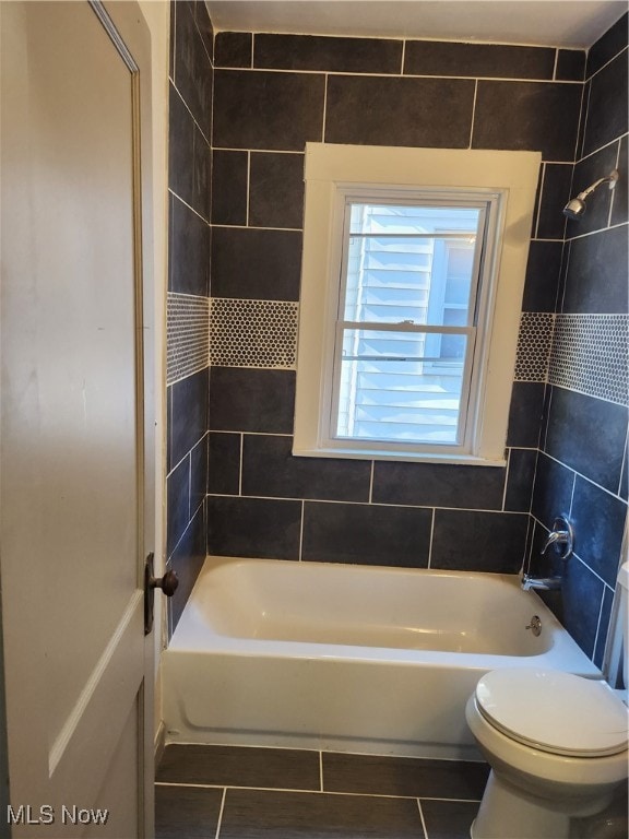 bathroom featuring tile patterned flooring, tiled shower / bath combo, toilet, and tile walls