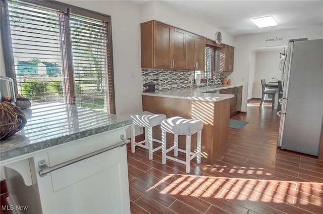 kitchen featuring dark wood-type flooring, sink, stainless steel fridge, kitchen peninsula, and a breakfast bar area