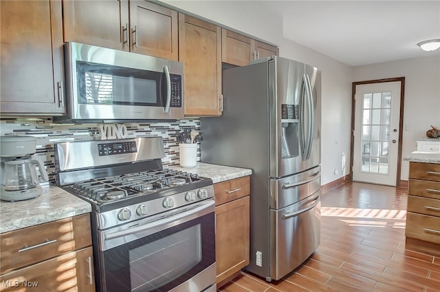 kitchen with tasteful backsplash, light stone counters, light hardwood / wood-style flooring, and appliances with stainless steel finishes