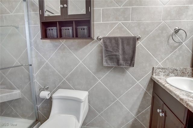 bathroom with vanity, a shower with shower door, tile walls, and toilet