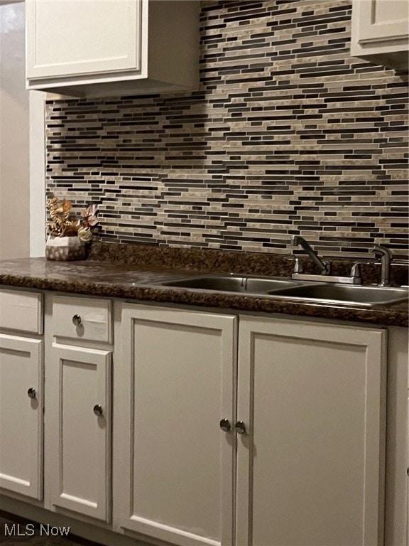 interior details with backsplash, white cabinetry, and sink