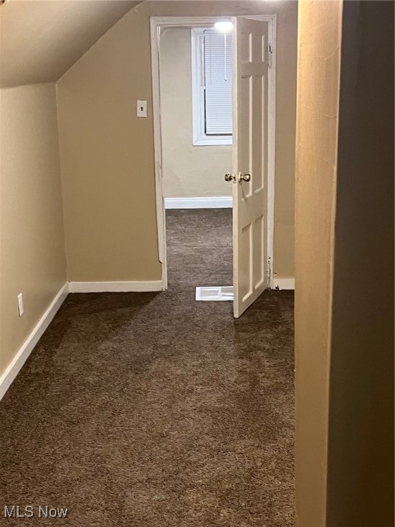 additional living space with dark colored carpet and vaulted ceiling