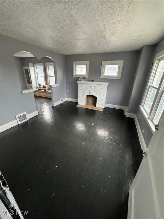 unfurnished living room featuring a brick fireplace, dark wood-type flooring, and a textured ceiling