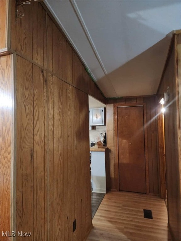 hall with light wood-type flooring, vaulted ceiling, and wooden walls