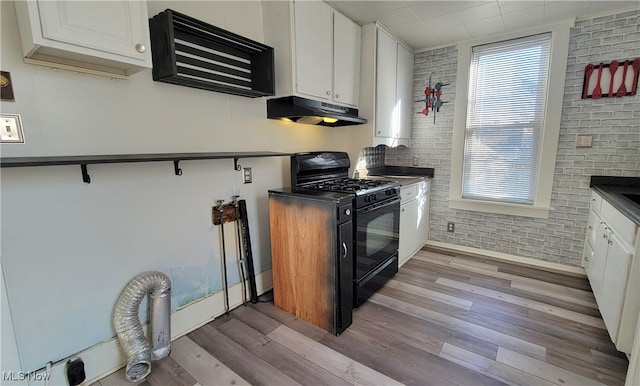 kitchen featuring white cabinets, black range with gas cooktop, and brick wall