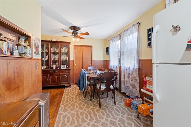 dining space featuring ceiling fan, wooden walls, and dark hardwood / wood-style floors