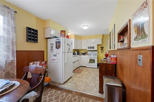 kitchen with wood walls, white cabinets, white appliances, and light wood-type flooring