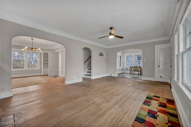 unfurnished living room with ceiling fan with notable chandelier, crown molding, a wealth of natural light, and light hardwood / wood-style flooring