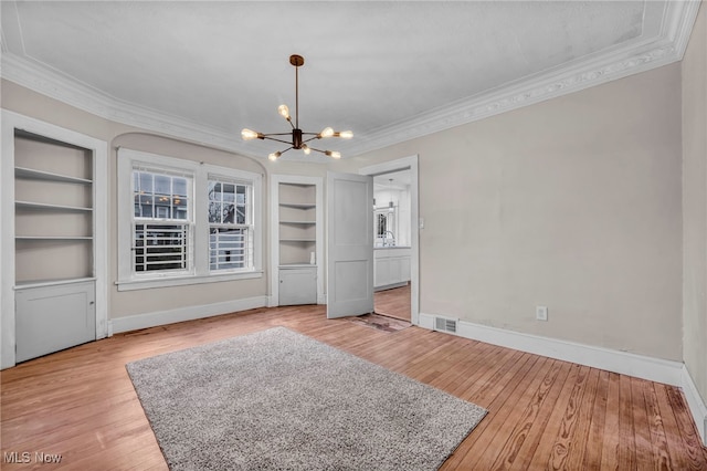 interior space featuring built in shelves, light wood-type flooring, ornamental molding, and an inviting chandelier