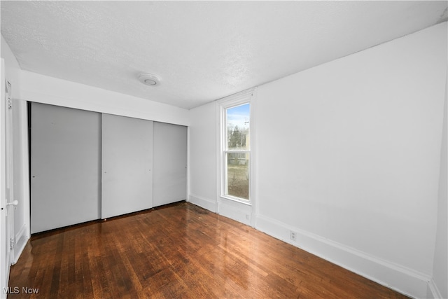 unfurnished bedroom featuring a textured ceiling, a closet, and dark hardwood / wood-style floors