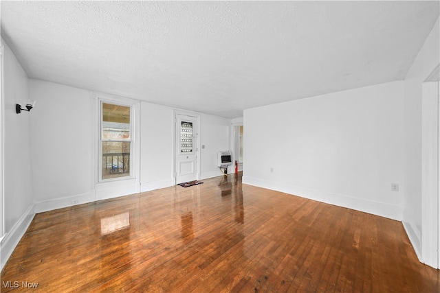 empty room featuring heating unit, wood-type flooring, and a textured ceiling