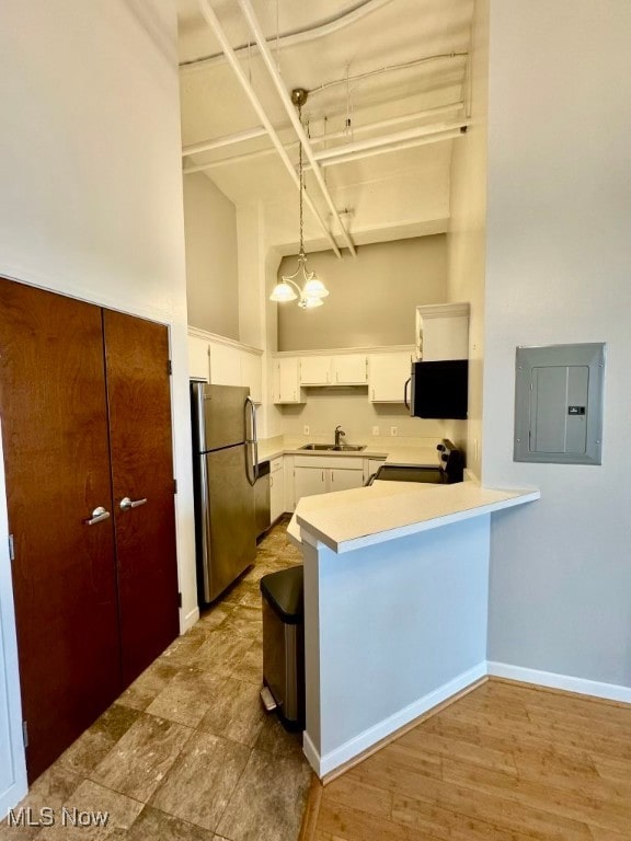 kitchen featuring stainless steel refrigerator, electric panel, white cabinets, and hanging light fixtures