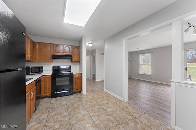 kitchen with a skylight, a wealth of natural light, black appliances, and light wood-type flooring