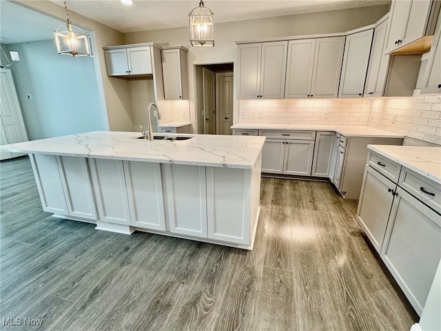 kitchen with an island with sink, wood-type flooring, and decorative light fixtures