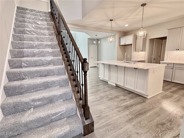 kitchen with light wood-type flooring, tasteful backsplash, pendant lighting, a center island with sink, and white cabinetry