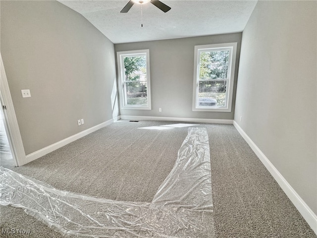 carpeted spare room featuring a textured ceiling, vaulted ceiling, plenty of natural light, and ceiling fan