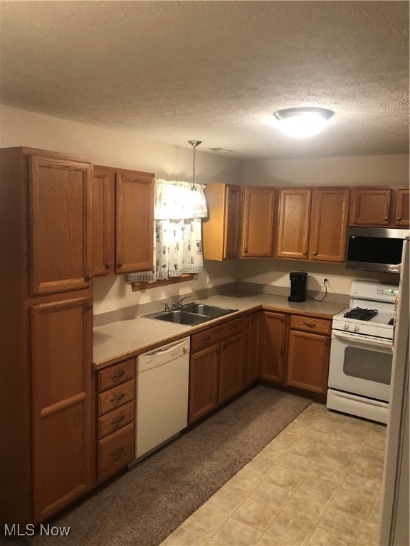 kitchen with a textured ceiling, sink, white appliances, and hanging light fixtures