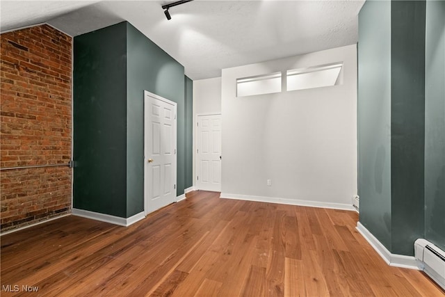 unfurnished room featuring hardwood / wood-style floors, brick wall, a textured ceiling, and a baseboard heating unit