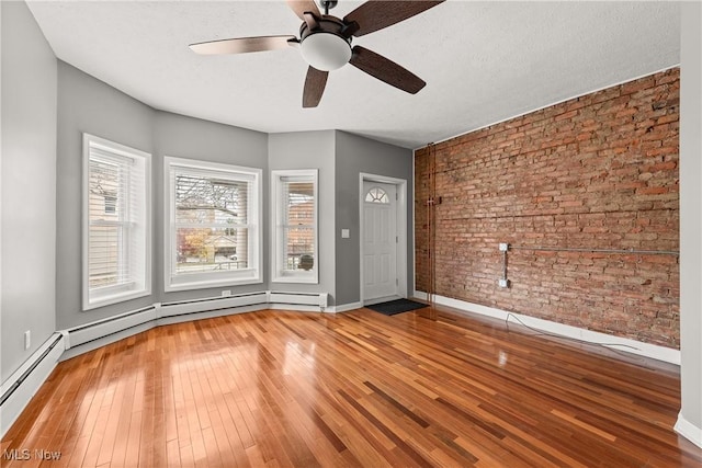 unfurnished room featuring hardwood / wood-style floors, ceiling fan, a textured ceiling, and brick wall