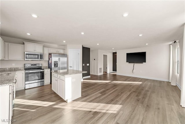 kitchen with stainless steel appliances, a kitchen island, light stone counters, white cabinets, and light wood-type flooring