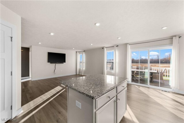 kitchen featuring stone countertops, a kitchen island, a textured ceiling, and light hardwood / wood-style flooring