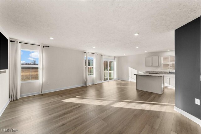 unfurnished living room with a textured ceiling, a wealth of natural light, and light hardwood / wood-style flooring