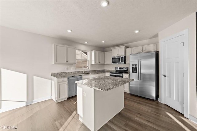 kitchen featuring light stone countertops, appliances with stainless steel finishes, dark wood-type flooring, sink, and a center island