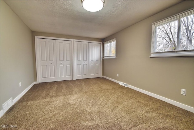 unfurnished bedroom with carpet, a textured ceiling, and two closets