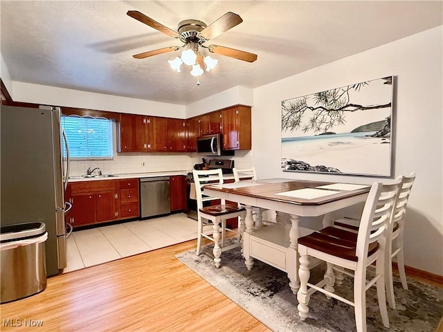 kitchen featuring appliances with stainless steel finishes, sink, backsplash, ceiling fan, and light hardwood / wood-style floors