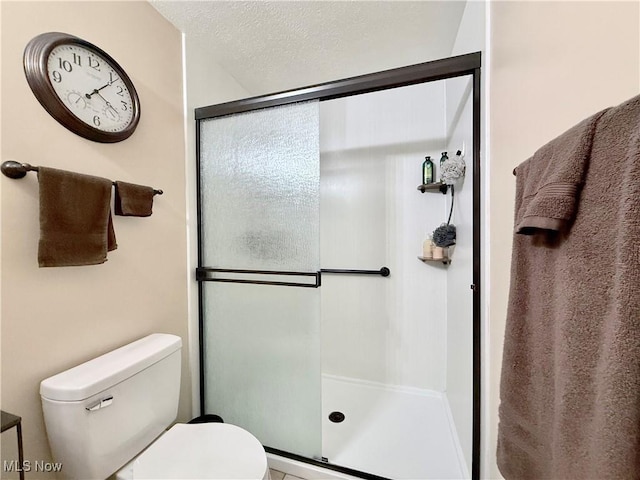 bathroom featuring a textured ceiling, a shower with door, and toilet