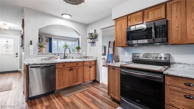 kitchen featuring sink, stainless steel appliances, light stone counters, dark hardwood / wood-style floors, and a textured ceiling