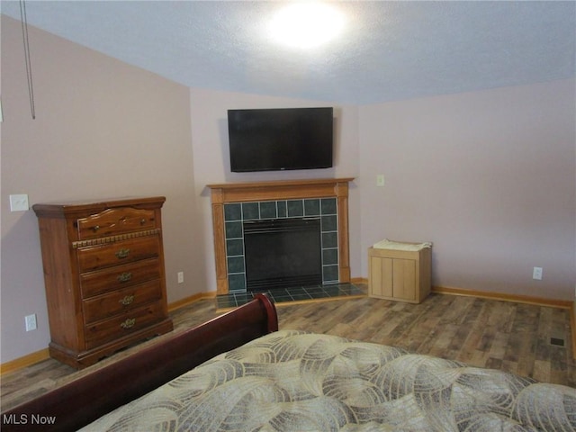 bedroom with a tiled fireplace and hardwood / wood-style flooring