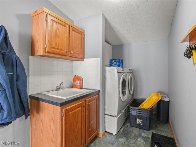 laundry room with a textured ceiling, washing machine and dryer, cabinets, and sink