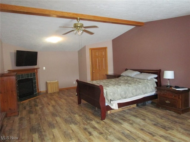 bedroom featuring wood-type flooring, lofted ceiling with beams, ceiling fan, and a tiled fireplace