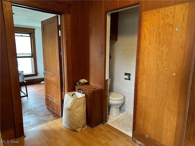 bathroom with hardwood / wood-style flooring, toilet, a textured ceiling, and wooden walls