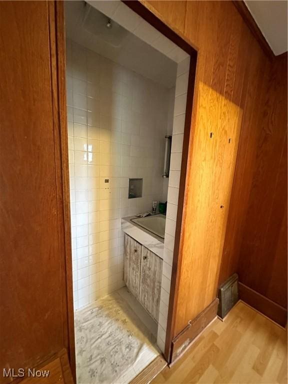 bathroom featuring wood walls, hardwood / wood-style floors, tile walls, and a washtub