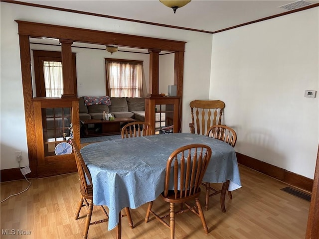 dining room featuring decorative columns, a wealth of natural light, light hardwood / wood-style flooring, and crown molding