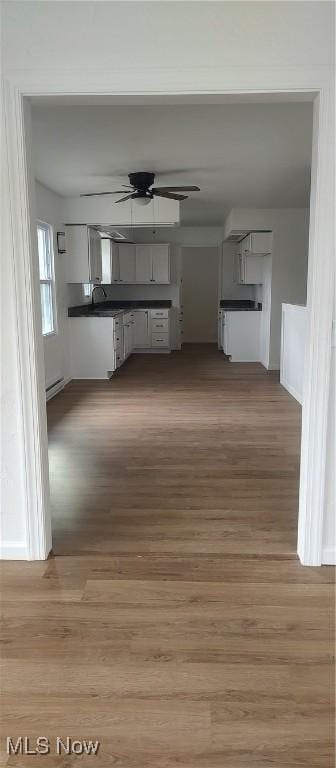 interior space with ceiling fan, sink, a baseboard radiator, wood-type flooring, and white cabinets