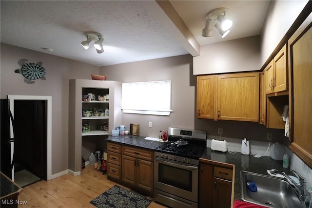 kitchen with light wood-type flooring, a textured ceiling, sink, and stainless steel range with gas stovetop