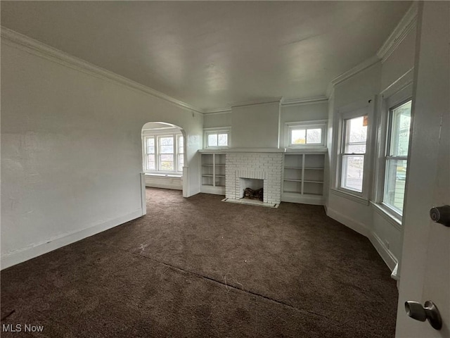 unfurnished living room with dark colored carpet, built in shelves, a fireplace, and crown molding