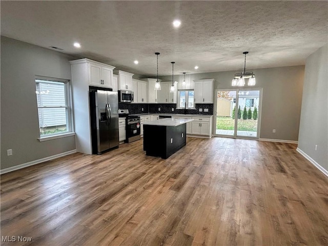 kitchen with appliances with stainless steel finishes, a kitchen island, hardwood / wood-style floors, white cabinetry, and hanging light fixtures