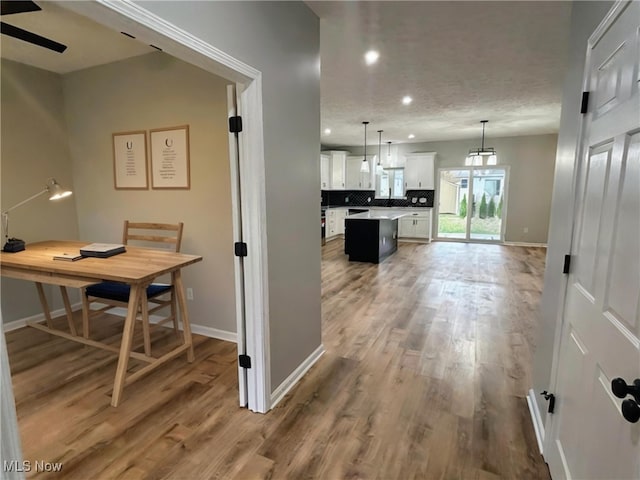 interior space with ceiling fan, wood-type flooring, decorative light fixtures, white cabinets, and a kitchen island