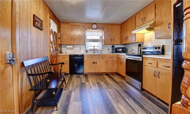 kitchen with sink, dark hardwood / wood-style floors, wooden walls, and black appliances