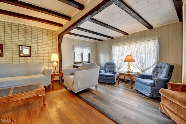 living area with beam ceiling, wood walls, and hardwood / wood-style floors