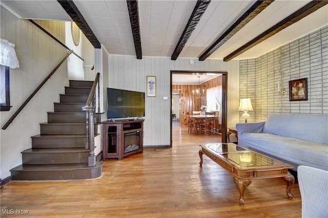 living room with beam ceiling, an inviting chandelier, wooden walls, and light hardwood / wood-style flooring