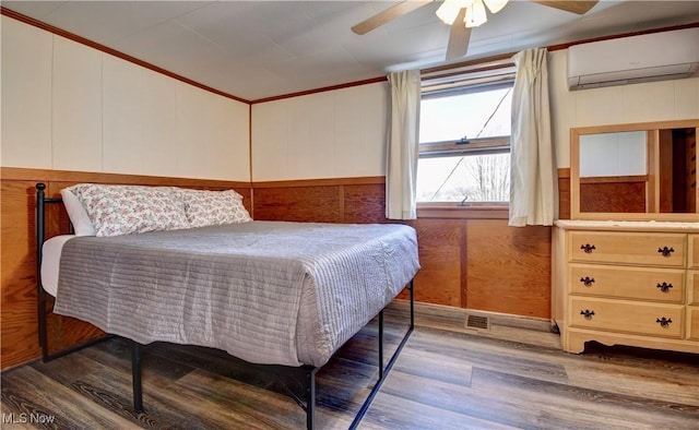 bedroom featuring dark wood-type flooring, crown molding, wooden walls, ceiling fan, and a wall unit AC