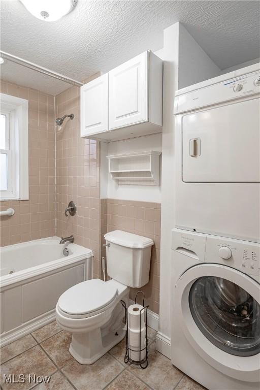 bathroom with a textured ceiling, tile patterned floors, tiled shower / bath, and stacked washer and clothes dryer